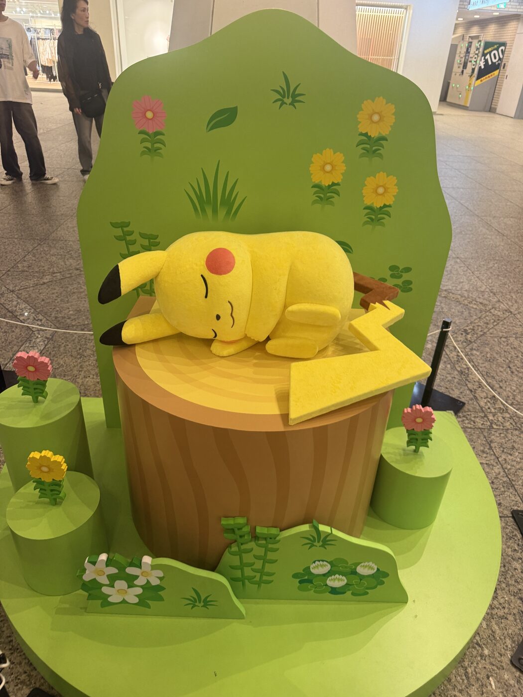 Pikachu asleep on a tree stump surrounded by flowers