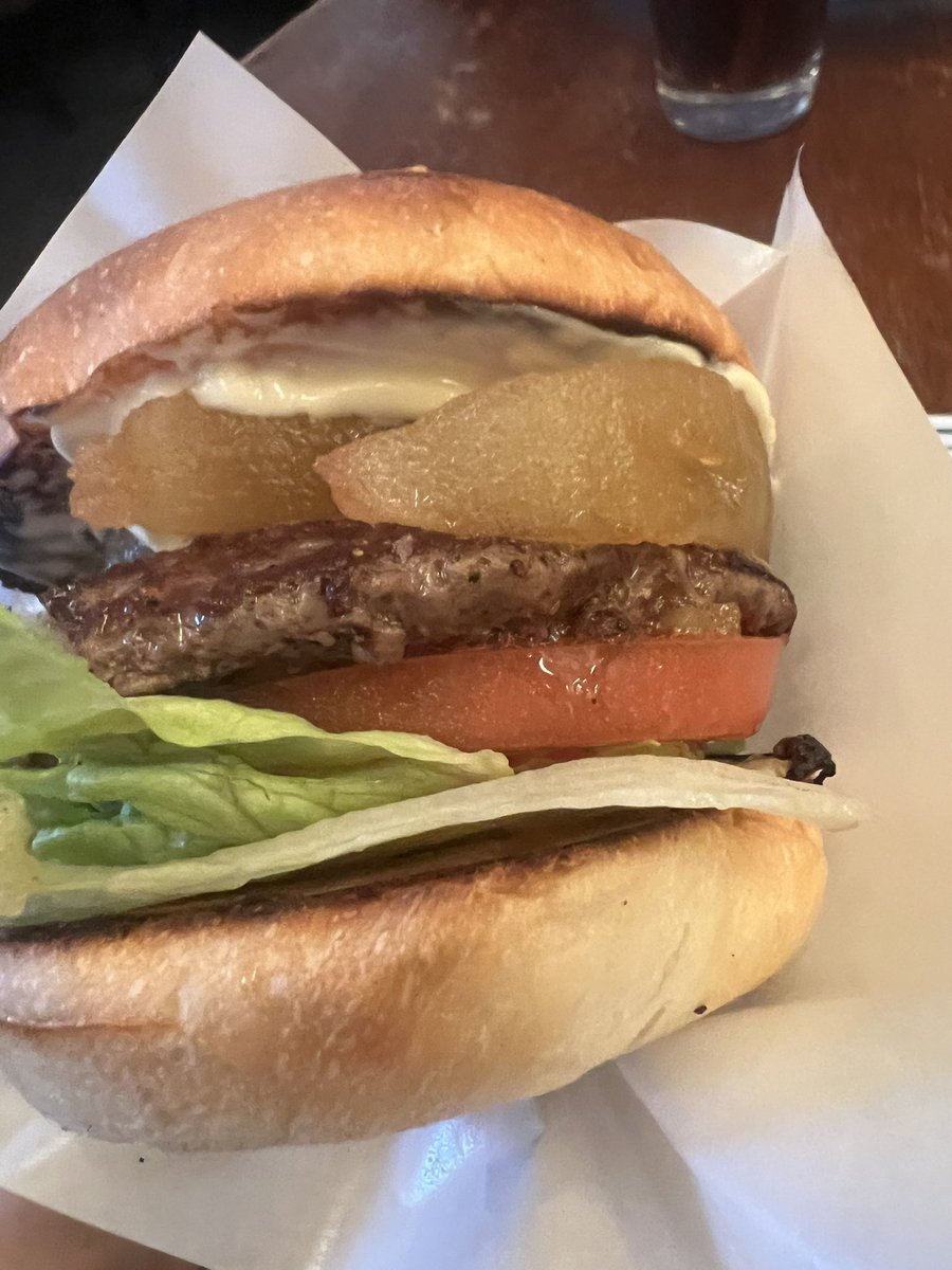 Close-up inside the Apple Burger showing the beef patty topped with translucent cinnamon-stewed apple, tomato and lettuce
