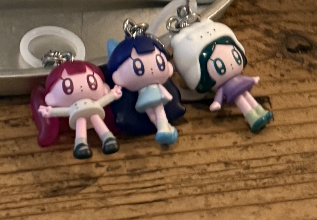 Three small chibi capsule-toy charm figures on a wooden café table