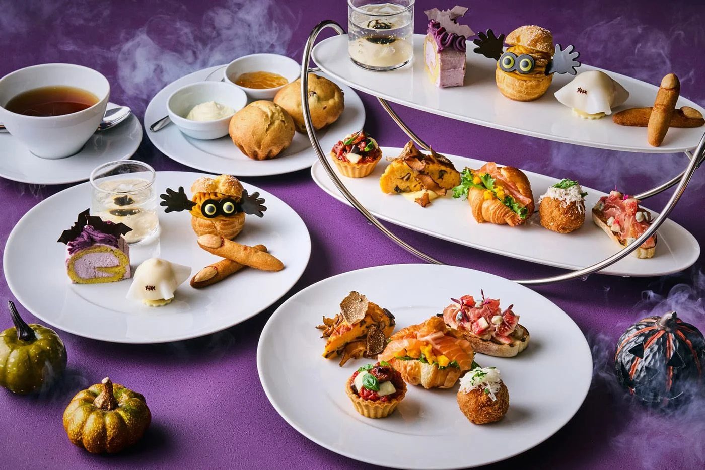 A Halloween afternoon tea spread at Grand Hyatt Tokyo — a tiered stand and plates of themed savouries and sweets, including a mummy choux, on a purple table with dry-ice mist