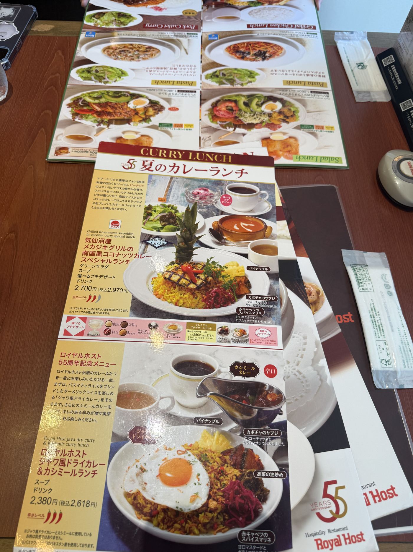 Royal Host menu cards on the table, including a summer curry lunch page and a 55th anniversary menu page with a dry curry topped with a fried egg