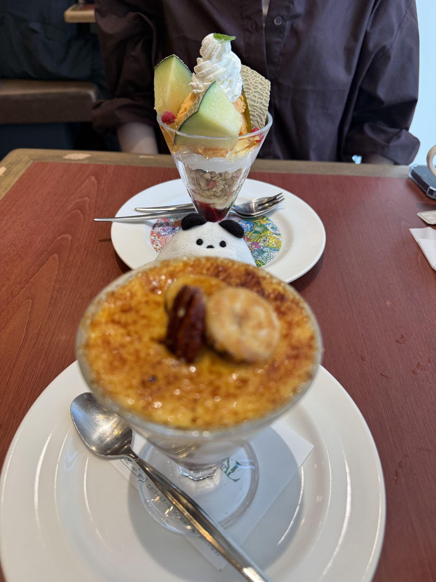 A brûlée parfait with a caramelised top, a pecan and fruit in the foreground, and a melon parfait topped with cream and a wafer behind it