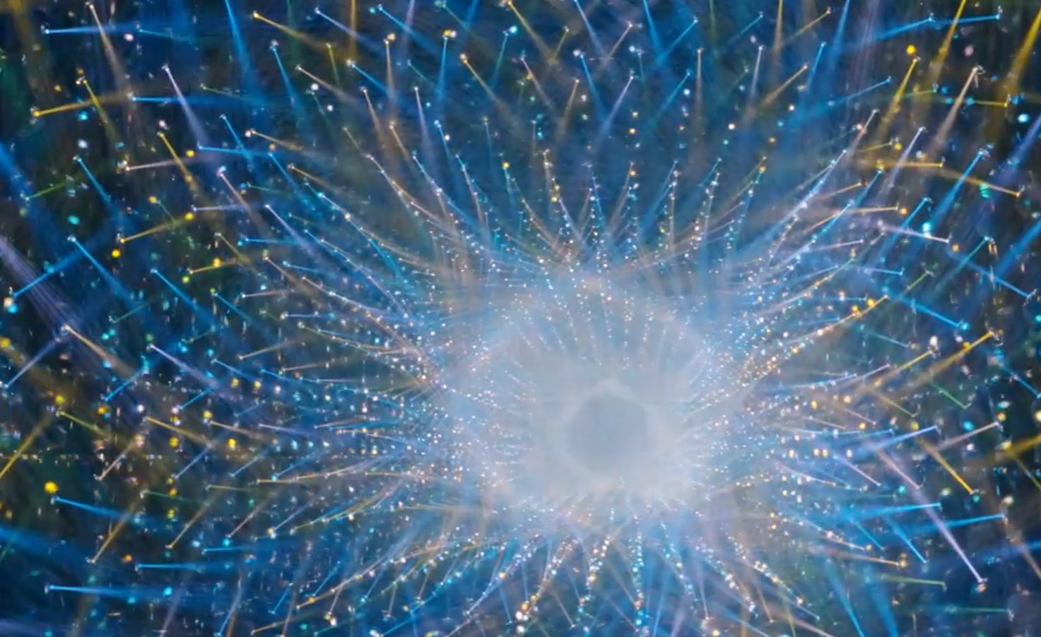A sphere of blue and gold points of light radiating outward in a dark mirrored room at teamLab Borderless